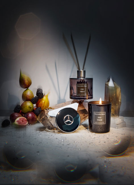 Merecdes-Benz Raumduft Collection. Abgebildet wird die Mercedes-Benz Raumduft Collection mit Kerze und Diffuser. Die Artikel sind in einem dunkleren Set dargestellt mit Lichteffekten und Kristallen sowie Feigen als Dekoelemente.