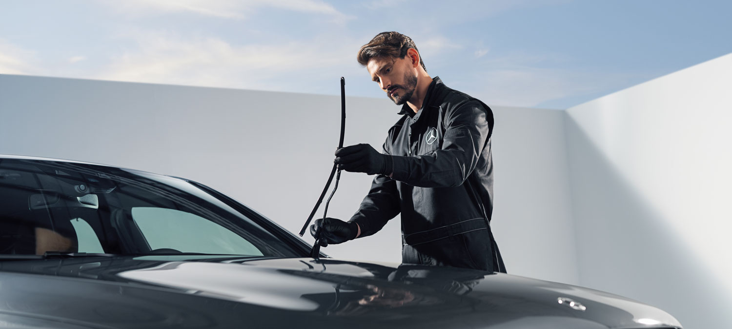 Mercedes-Benz Wischerblätter Ein Mitarbeiter prüft die montierten Mercedes-Benz Wischerblätter. Von dem Fahrzeug ist die Frontscheibe und ein Teil der Motorhaube zu erkennen, der Hintergrund ist hell.
