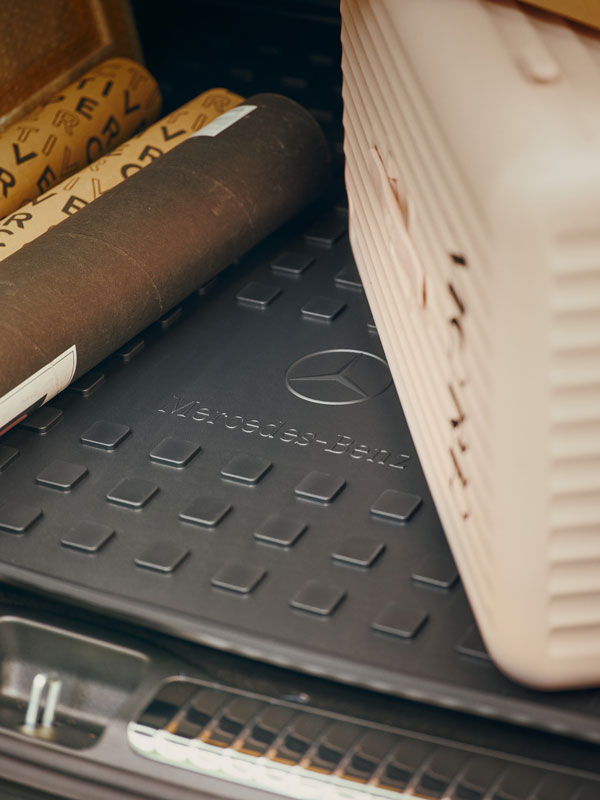 Mercedes-Benz Kofferraumwannen Im Bildausschnitt liegt eine Mercedes-Benz Kofferraumwanne im Kofferraum. Dieser wurde beladen mit einem beigen Koffer und mehreren Papprollen.