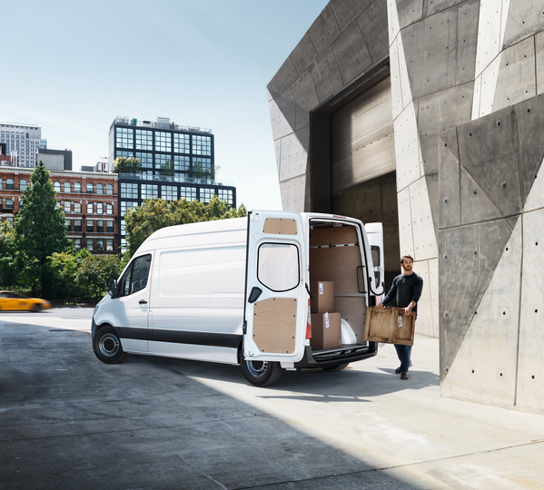 Ein weißer Mercedes Sprinter wird mit Paketen beladen.